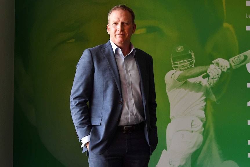 An Australian cricket executive stands in front of a photo portrait of Ricky Ponting.