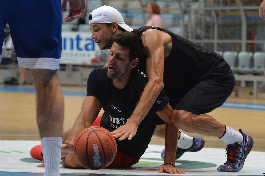 Grigor Dimitrov and Novak Djokovic wrestle as they try to get to a basketball.