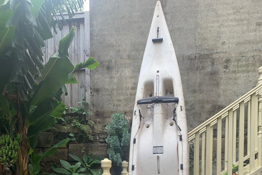 A white Wave Witch Kayak leaning on pale yellow stairs in a backyard.