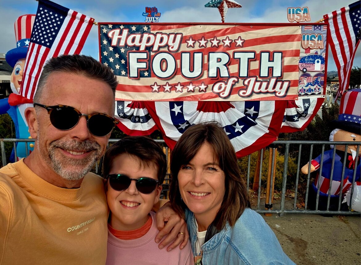 A man, woman and young son in front of a Happy Fourth of July sign.
