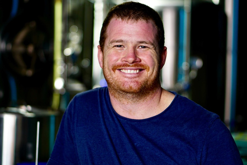 A close up of a man in a blue t-shirt smiling at the camera.