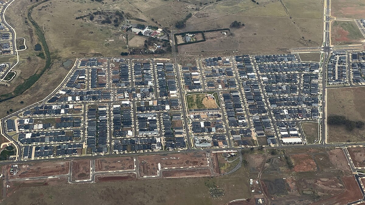 Un disparo aéreo mirando a las casas suburbanas de techo negro bordeadas por potreros vacíos.