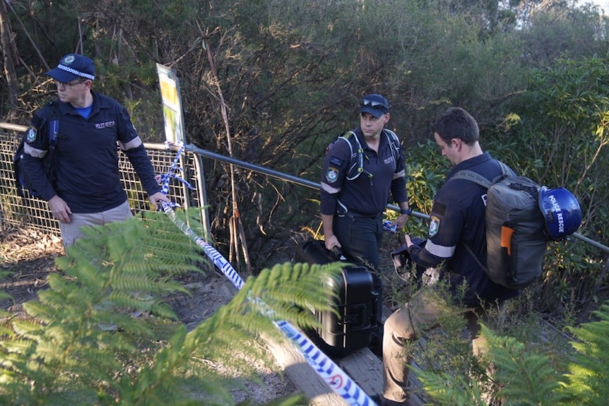 Three people standing near police rope in a bush 