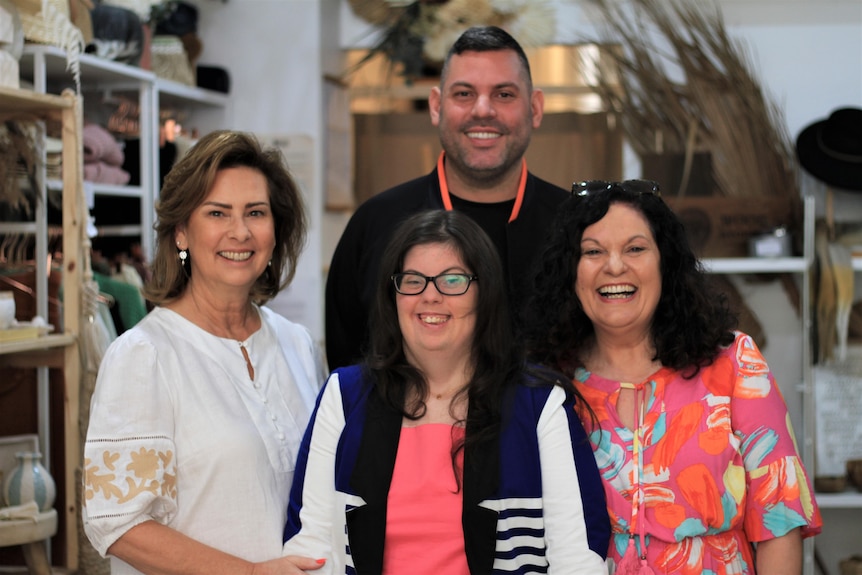 Four people stand in a retail store & smile, Simone wears a hot pink shirt, blue & white blazer & black glasses. 