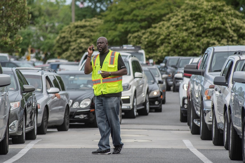 Cars queue for petrol in the US amid a fuel shortage, while an attendant supervises.