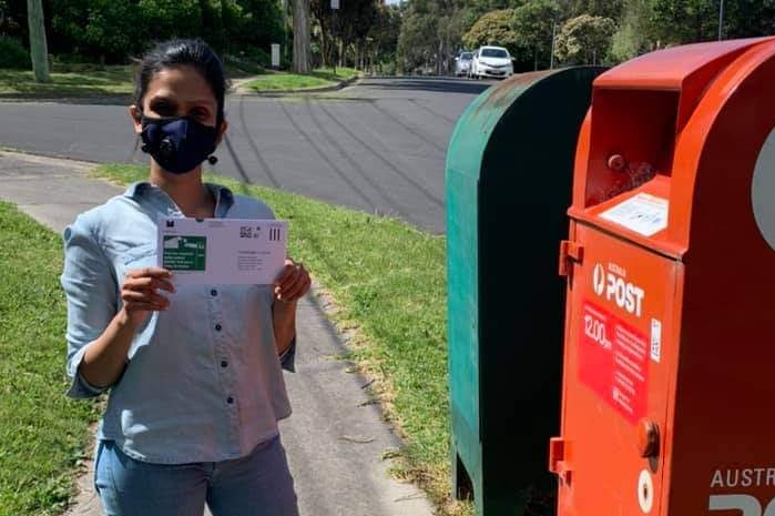 Anjalee de Silva wears a mask and holds her postal vote at the letter box.