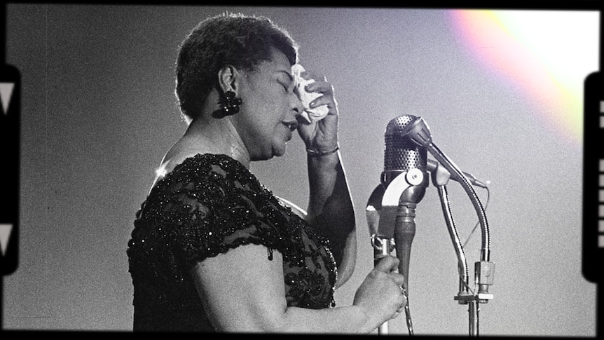 A monochrome photo of Ella Fitzgerald on-stage with some microphones