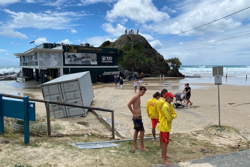 Three lifesavers and other people look at the high tide at Currumbin surf cub. 