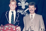 A younger man and an older man pose with trophies.