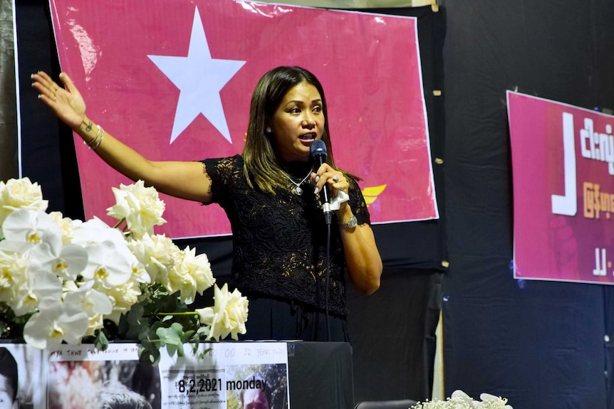 A woman speaks into a microphone with her arm raised