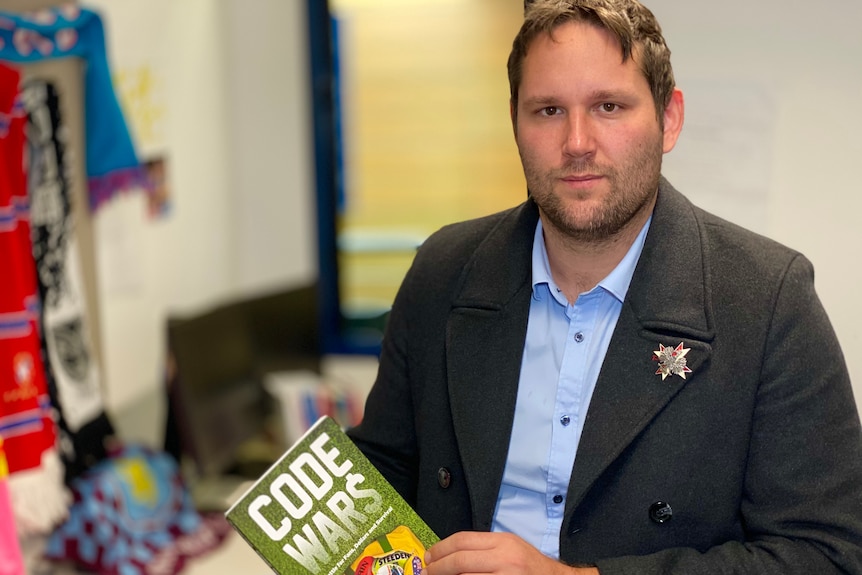 A man stands in an office holding a book