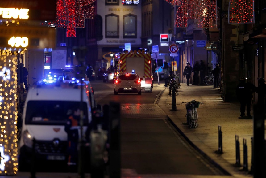 Emergency vehicles and workers on a street with Christmas lights where a shooting happened.