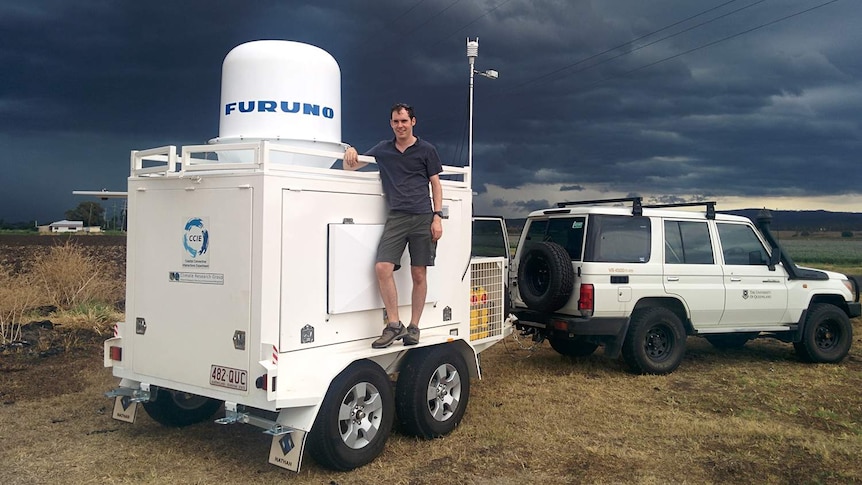 Dr Joshua Soderholm stands on a trailer loaded with weather instruments.