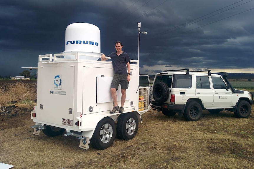 Dr Joshua Soderholm stands on a trailer loaded with a weather station.