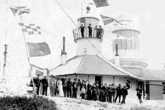A black and white photo showing the opening of a new lighthouse with an older lighthouse in the foreground
