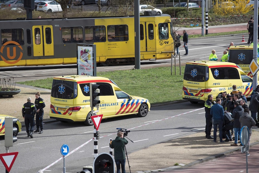 The tram is stopped and multiple ambulances are parked in the street as people look on.