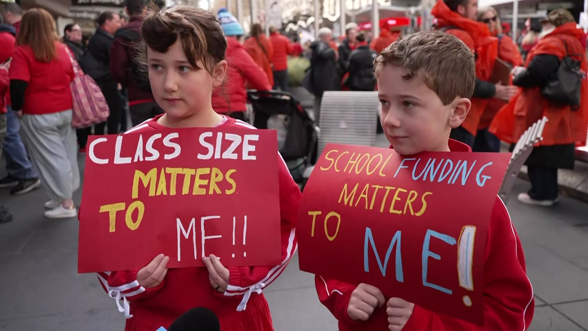 A girl and a boy are dressed in red and hold posters calling for a teachers' rally.