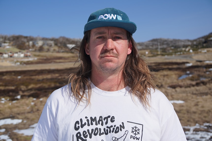 A long haired man looks seriously into the camera with a blue hat.