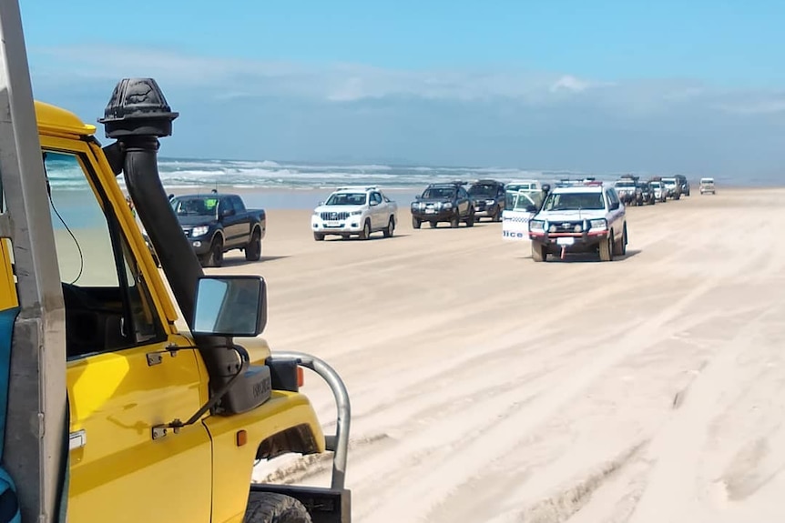 Line of four wheel drives along the beach with police driving along side