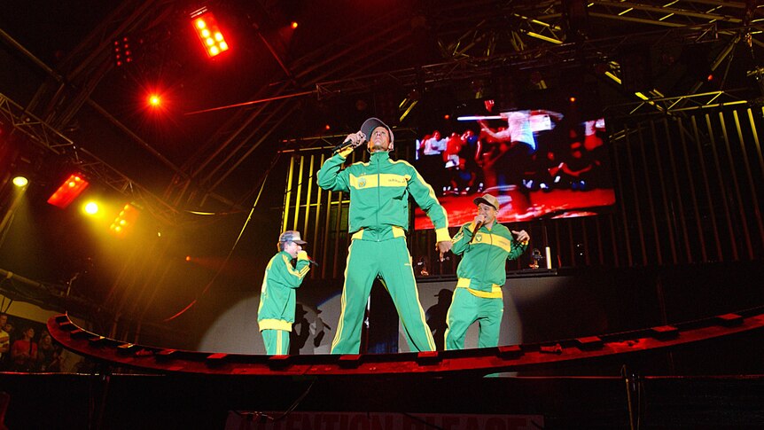 Beastie Boys wear green and gold tracksuits as they rap on a large stage