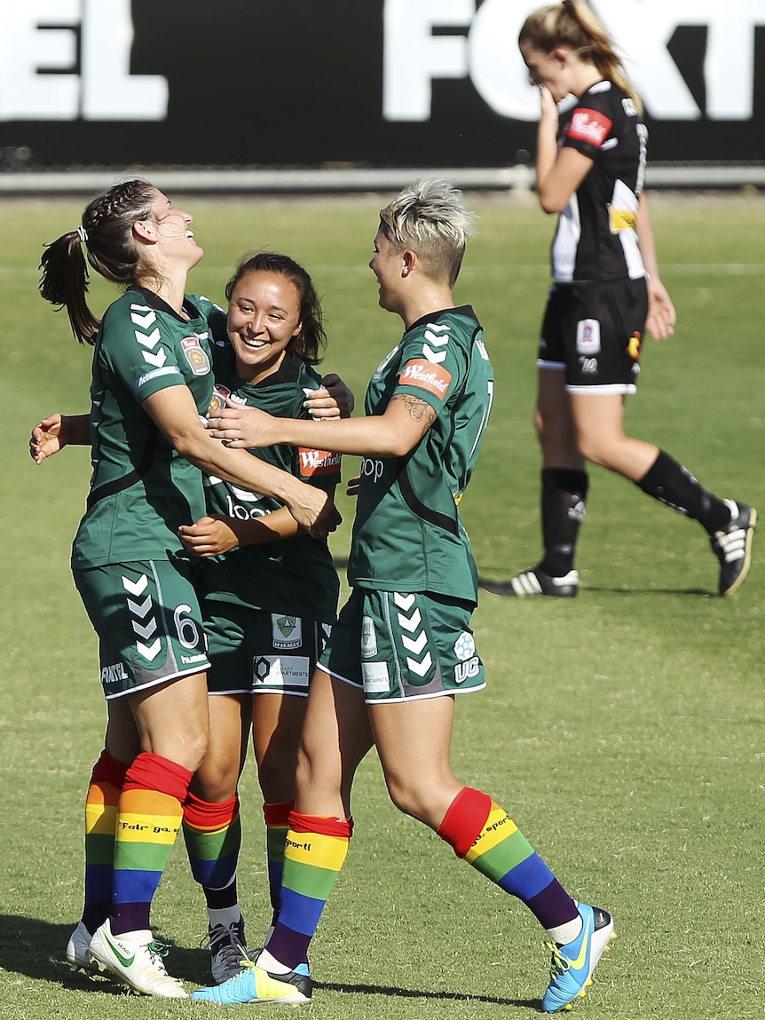 Women soccer players wearing green and rainbow socks celebrate a goal