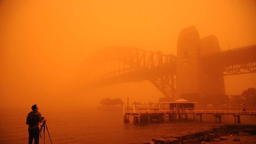 A photographer standing below Sydney Harbour Bridge during a dust storm, with everything coloured orange.