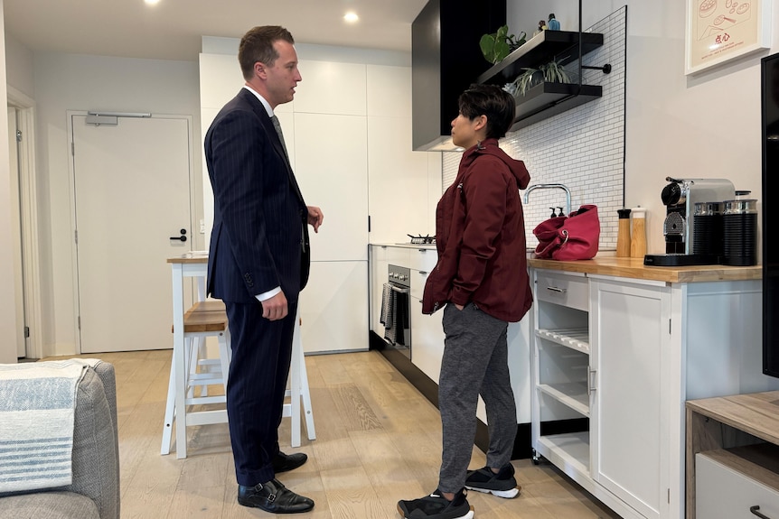 a man in a suit talking to a person in a small kitchen