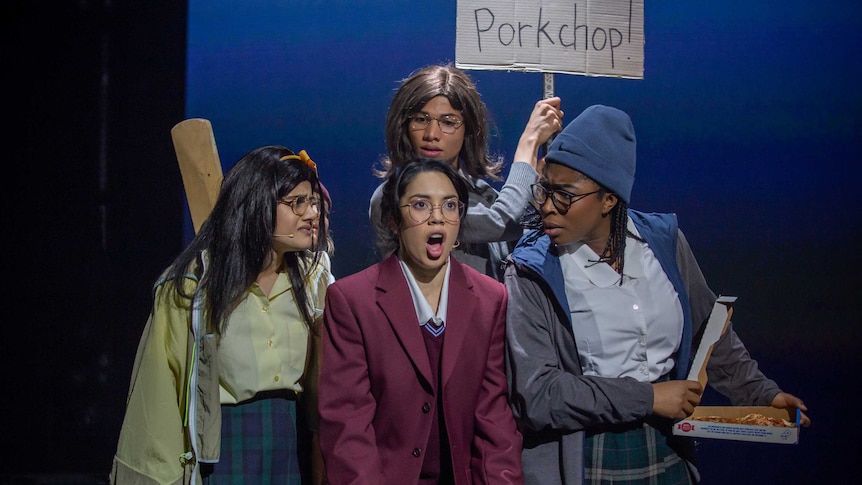 Four actors dressed in high school uniforms singing on stage.