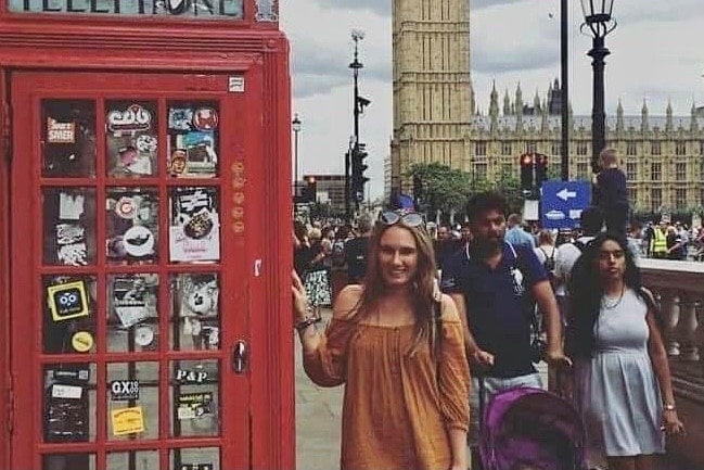 A woman stands next to a red telephone box