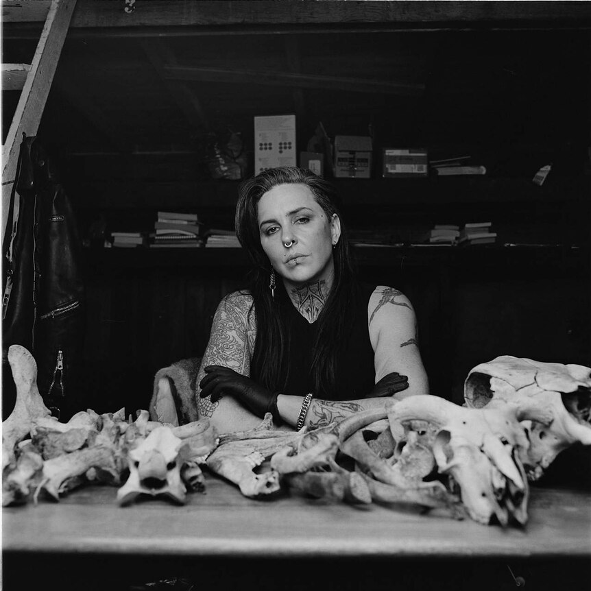 S.J Norman sits at a table in their studio. On the table in front of them are bones collected from Walgalu Country.