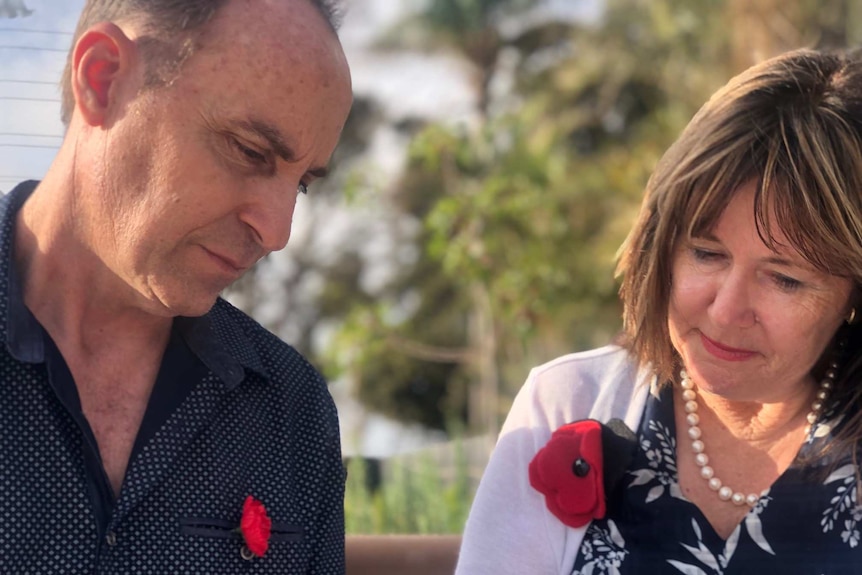 A man and a woman, wearing red poppies for remembrance