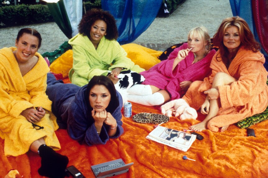 The Spice Girls in brightly coloured robes: Mel C in yellow, Victoria in purple, Mel B in green, Emma in pink, Geri in yellow