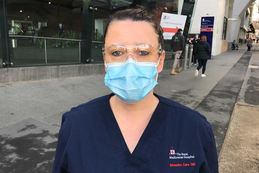 A women wearing a blue surgical mask and dark blue scrubs.