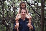 A daughter smiles as she sits on her dad's shoulders on Fraser Island.