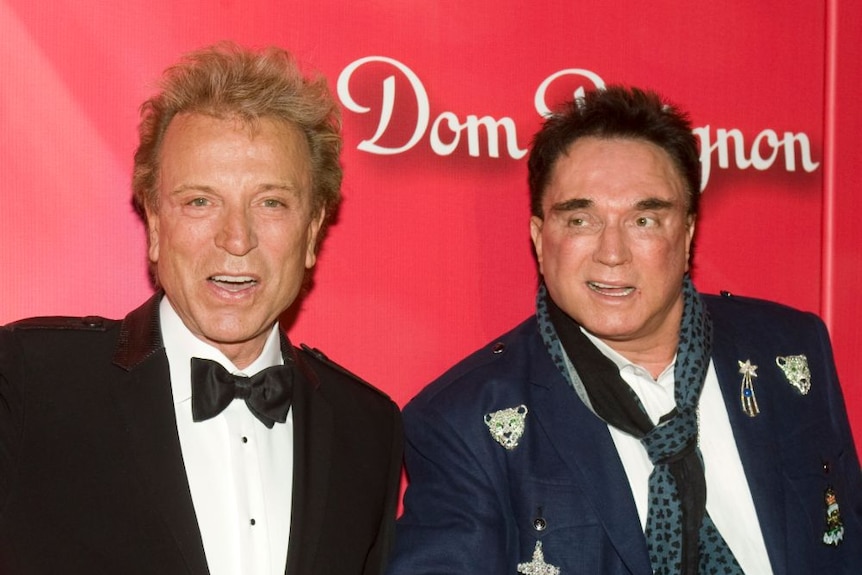 Siegfried and Roy look at the camera in front of a red background