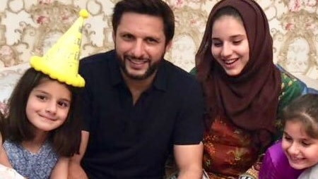 Shahid Afridi sits next to his wife and two of his children with a brown cake in front of them