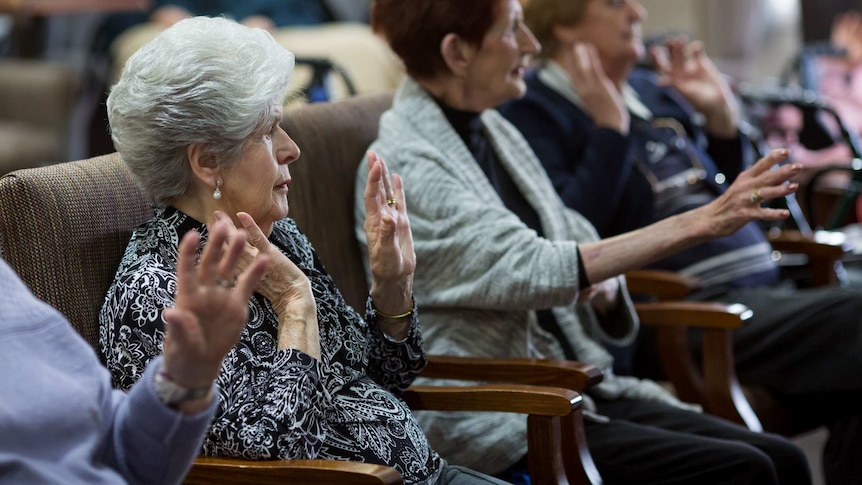 Aged care resident Nancy Gurciullo sitting in a chair with her hands held up in front of her.