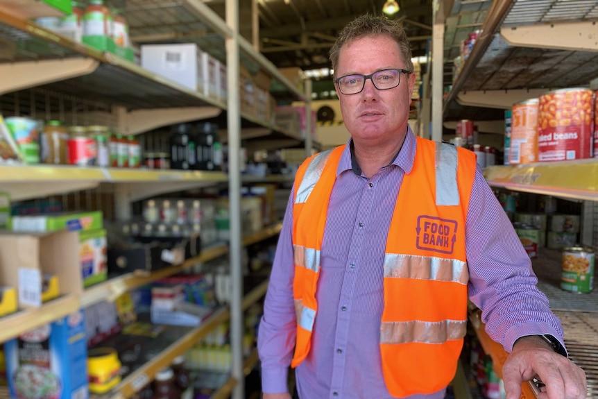 Peter Pilt stands in the Foodbank storage area, cans of food can be seen behind him.