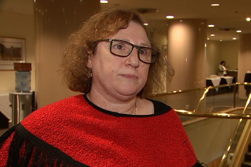 Nadia Moffatt wearing black glasses and a red jumper in front of a staircase