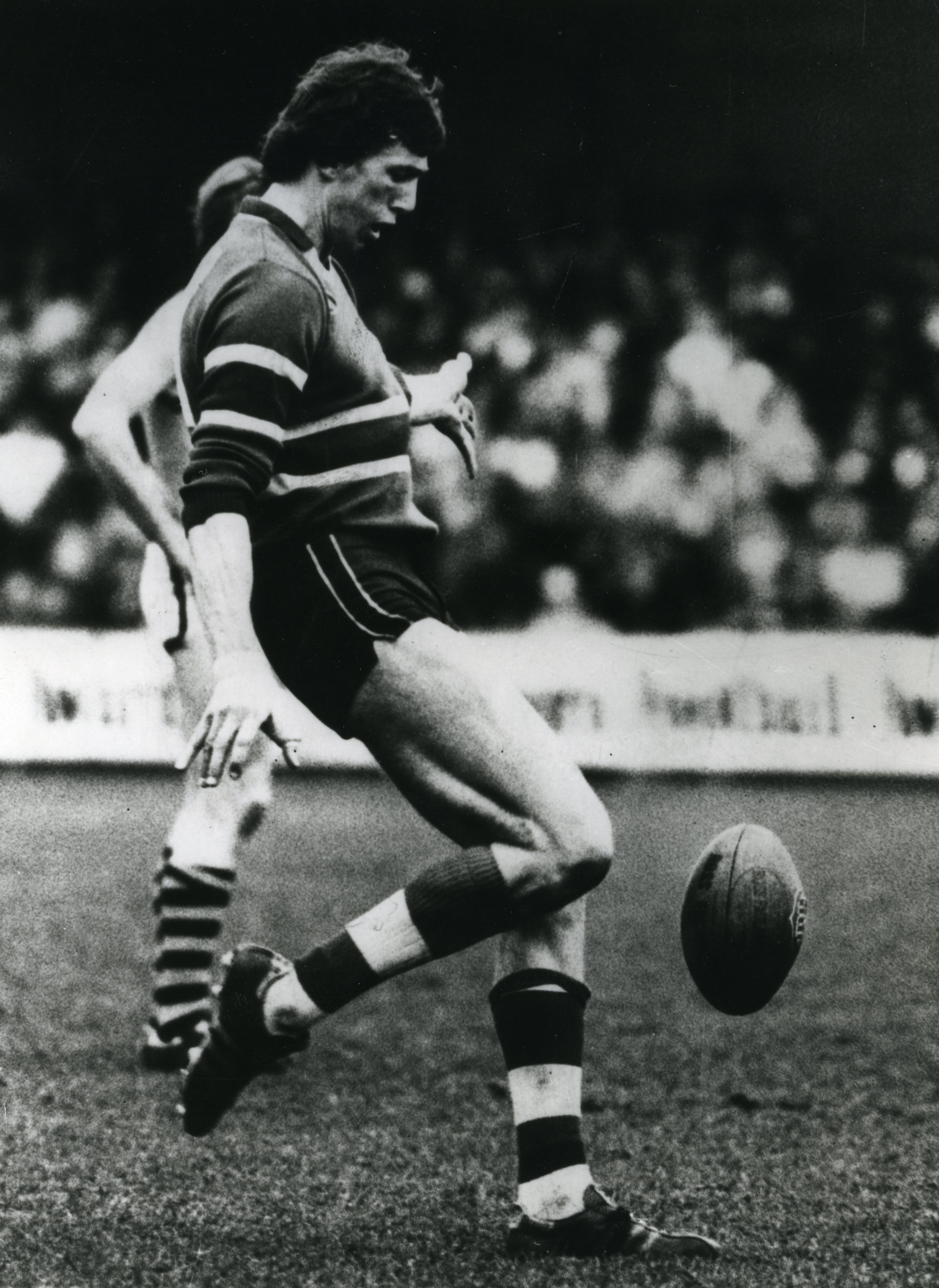 Uma foto em preto e branco de um jogador de futebol da VFL chutando a bola.