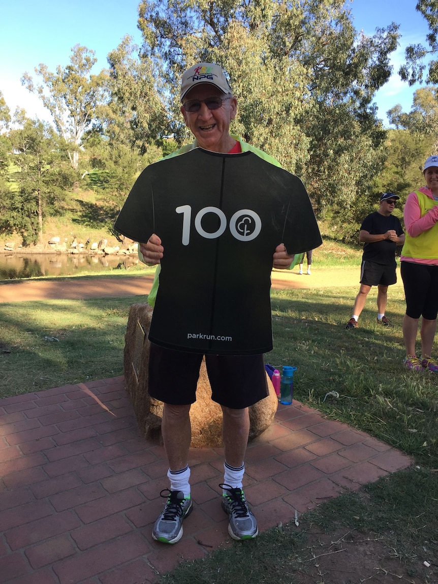 A man smiling with a sign with the number "100" on it