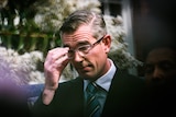 A man touching his glasses in a suit