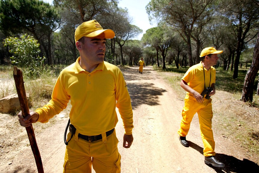 Two men in bright yellow uniforms walking down a dirt road 
