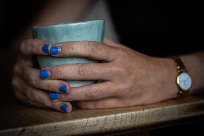A woman's hands with blue painted nails holds a mug