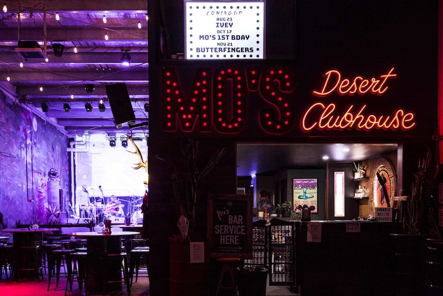 El interior de un club nocturno, con un letrero de neón que dice Moe's Desert Clubhouse.