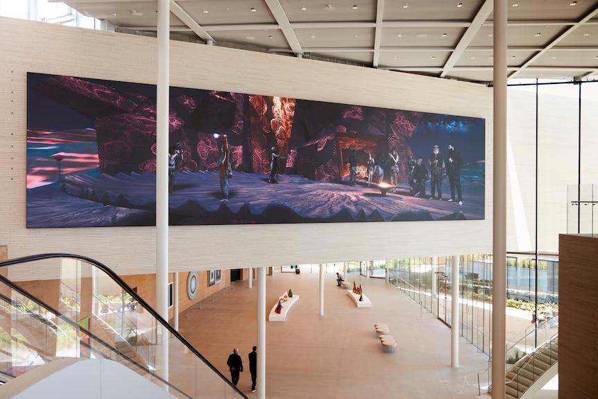 The foyer of a modern gallery with a large colorful artwork hanging, the artwork depicts Indigenous people in a sci-fi setting