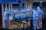 Health workers in hazmat suits wheel a person sealed inside a stretcher into a hospital
