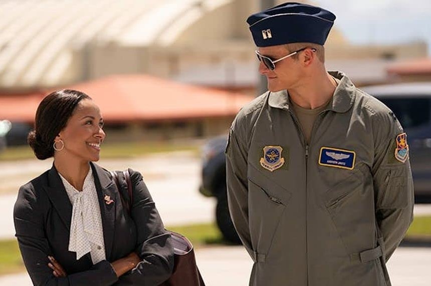 Kat Graham crosses her arms across her chest while looking across at Alexander Ludwig in Air Force uniform.