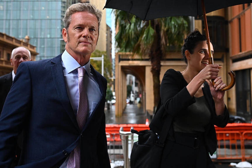 a man walking outside while a woman holds an umbrella over his head