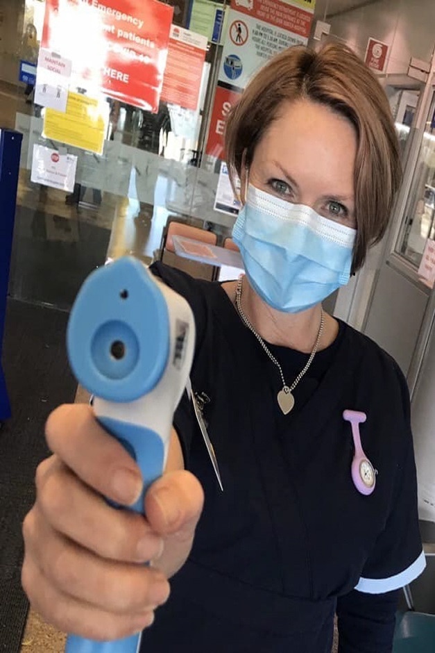 Woman in face mask putting thermometer at camera